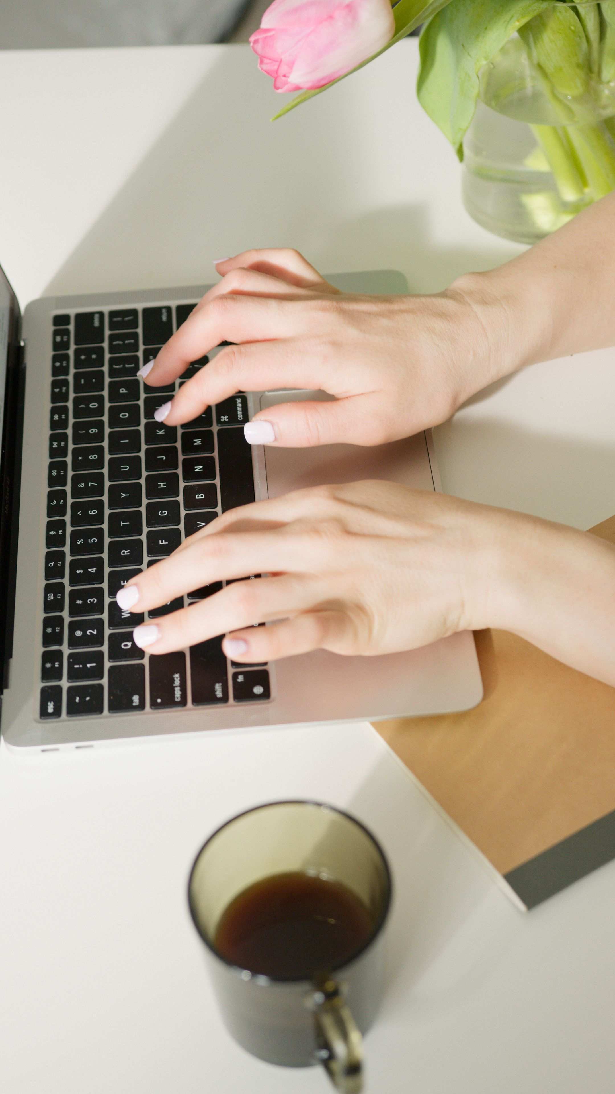 Hände beim Tippen auf einer Laptop-Tastatur, in der Nähe ein Kaffeebecher auf dem Schreibtisch